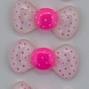 May include: Four pink and white polka dot bows with a pink center. The bows are made of a clear plastic material with pink polka dots.