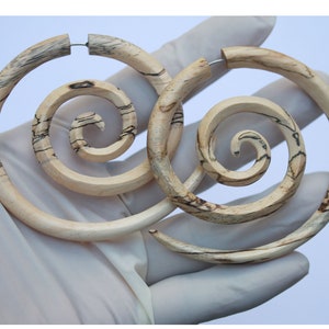 May include: A pair of wooden hoop earrings with a spiral design. The earrings are made of light brown wood with dark brown streaks.