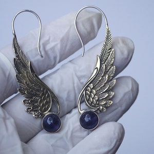 May include: A pair of silver earrings with gold wings and purple gemstones. The wings are detailed with intricate designs.