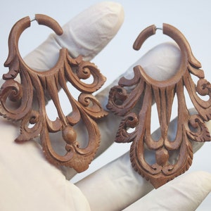 Könnte beinhalten: Ein Paar aufwendig geschnitzte Holzohrringe mit einem tropfenförmigen Design. Die Ohrringe sind braun und haben eine runde Form mit einem dekorativen Muster.