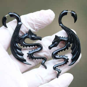 Puede incluir: Un par de expansores de oreja en forma de dragón negro. Los expansores están hechos de un material liso y pulido y presentan detalles intrincados.