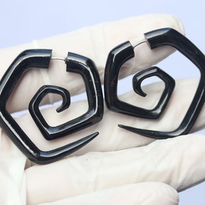 Op de afbeelding: Paar zwarte spiraalvormige hoorn oorringen met een vierkante vorm. De oorringen zijn gemaakt van natuurlijk hoorn en hebben een zilveren metalen ring.