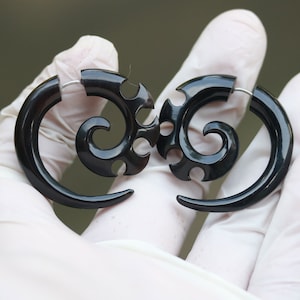 Op de afbeelding: Een paar zwarte spiraalvormige oorpluggen met ingewikkelde ontwerpen. De pluggen zijn gemaakt van een glad, gepolijst materiaal en hebben een glanzende afwerking.