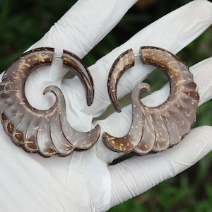 May include: A pair of brown, spiral-shaped earrings with a textured, layered design. The earrings are made of a natural material, possibly wood or coconut shell, and have a silver-coloured metal post for piercing.