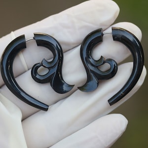 Könnte beinhalten: Ein Paar schwarze Horn-Ohrstecker mit einem dekorativen floralen Design. Die Stecker sind aus natürlichem Horn gefertigt und haben eine glatte, polierte Oberfläche.