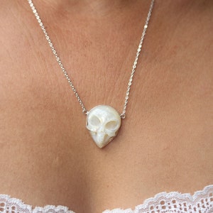 May include: A silver chain necklace with a white, pearlescent skull pendant.