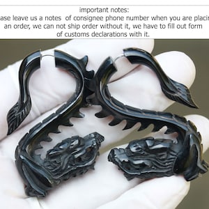 Peut inclure: Une paire de jauges d'oreille en forme de dragon noir en corne. Les jauges sont incurvées et présentent un motif de dragon détaillé.