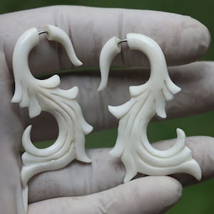 Könnte beinhalten: Ein Paar weiße Knochenohrringe mit floralem Design. Die Ohrringe sind hakenförmig und haben ein zartes, filigranes Design.