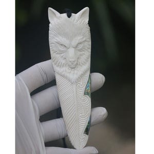 May include: White carved wolf pendant with abalone shell inlay. The wolf's face is detailed and the pendant is shaped like a feather.
