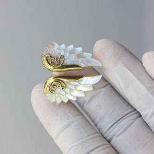 May include: A decorative cuff bracelet featuring a wing design. The wings are made of white iridescent material, with gold-colored metal accents. The bracelet is designed to wrap around the wrist.