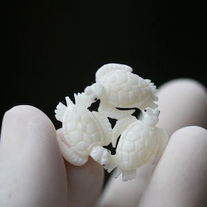 May include: Three white carved sea turtle figurines, arranged in a cluster, with intricate details on their shells and heads.
