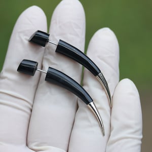 Op de afbeelding: Twee zwarte hoornvormige oorbellen met zilveren steentjes. De oorbellen worden getoond op een wit oppervlak.