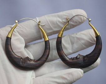 May include: A pair of wooden earrings shaped like crescent moons with gold accents. The earrings are dark brown with a wood grain pattern.