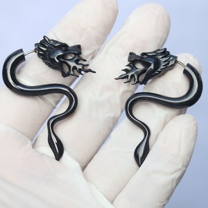 May include: A pair of black dragon head earrings with a curved, snake-like design. The earrings are made of a smooth, polished material.