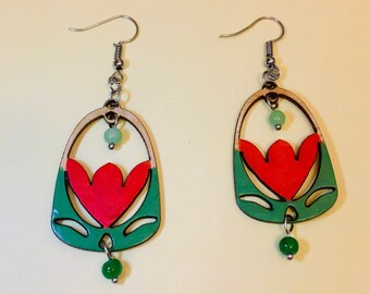 May include: A pair of wooden earrings with a red flower design, green accents, and green beads. The earrings are oval shaped and have a silver hook.