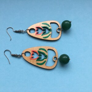 May include: A pair of wooden earrings with a green and orange floral design and a green bead dangle.