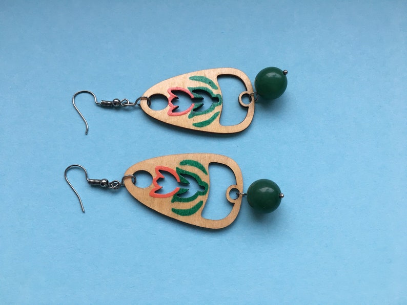 May include: A pair of wooden earrings with a green and orange floral design and a green bead dangle.