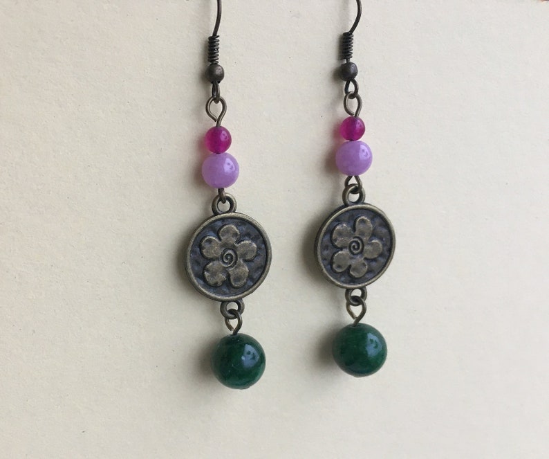 May include: A pair of dangle earrings with a flower charm, green, purple, and pink beads.
