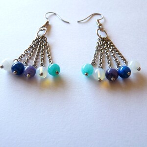 May include: A pair of silver dangle earrings with multiple chains and colorful gemstone beads. The beads are white, blue, purple, and turquoise.