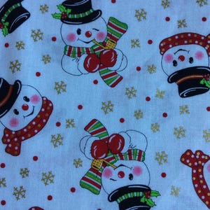 May include: White fabric with a repeating pattern of snowmen wearing black hats, red and white scarves, and holding candy canes. The background is white with gold snowflakes and red dots.