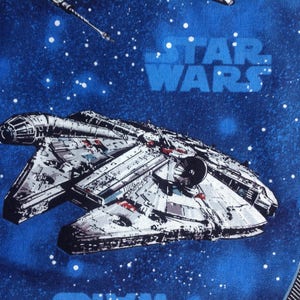 May include: A blue fabric with a white star field and the words "Star Wars" printed in white. The fabric features a spaceship in the center of the image.
