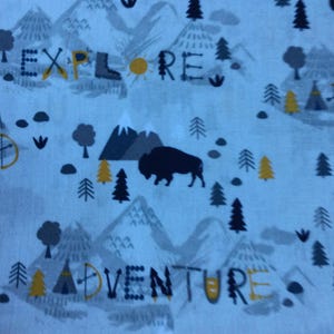 Könnte beinhalten: Ein weißer Stoff mit einem blauen und grauen Muster aus Bergen, Bäumen und einem Büffel. Der Stoff hat die Wörter "Explore", "Adventure", "Camp" und "Wild" aufgedruckt.