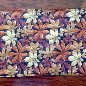 May include: A brown, gold, and cream table runner with a repeating pattern of stylized leaves. The leaves are arranged in a staggered pattern and are outlined in black.