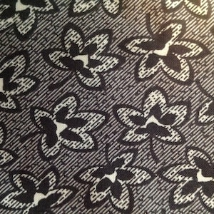 Może przedstawiać: Czarno-biała tkanina z powtarzającym się wzorem stylizowanych wzorów kwiatowych. Tkanina ma subtelną, fakturowaną powierzchnię.