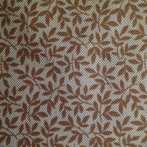 May include: A white fabric with a brown leaf pattern. The leaves are arranged in a repeating pattern and are a dark brown color.