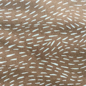May include: Close-up of a brown fabric with a repeating pattern of white, dash-like shapes. The dashes are irregularly spaced and oriented, creating a textured, organic appearance. The fabric has a woven texture.