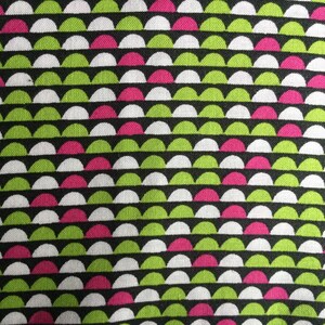 May include: Close-up of a fabric with a repeating pattern of semi-circles. The semi-circles are arranged in horizontal rows and alternate between white, lime green, and hot pink against a black background. The fabric has a textured appearance.