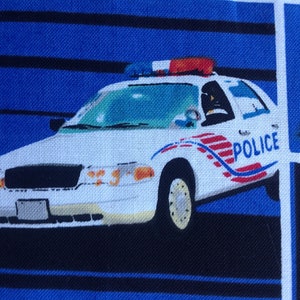 May include: A white police car with red and blue lights on top. The car has the word "POLICE" written on the side in red and blue letters. The car is on a blue and white striped background.