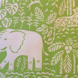 May include: A green and white fabric with a jungle-themed design. The pattern includes white elephants, leopards, and tropical plants. The fabric's design is a repeating pattern of these elements.