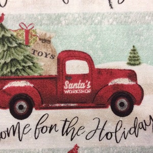 May include: A red vintage pickup truck with a Christmas tree, a bag of toys, and the words "Santa's Workshop" on the side. The truck is driving through a snowy scene with the words "Home for the Holidays" written below.