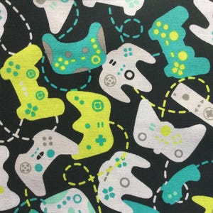 May include: Black fabric with a repeating pattern of video game controllers in white, teal, and yellow. The controllers are connected by dashed lines, creating a playful and modern design. The pattern is suitable for gaming enthusiasts.