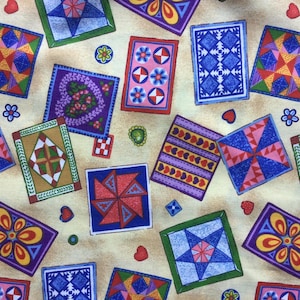 May include: A patterned fabric featuring a repeating design of colourful, square quilt blocks. The blocks display geometric and floral patterns in shades of blue, red, yellow, green, and purple, set against a beige background. Small hearts and flowers are scattered.