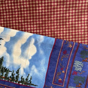Könnte beinhalten: Ein Stoff mit einem rot-weißen Gittermuster im oberen Bereich, das in einen blauen Himmel mit weißen Wolken und dunkelgrünen Kiefern auf der linken Seite übergeht, sowie einem blauen Rand mit kleinen Waldmotiven auf der rechten Seite.
