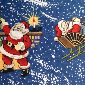 May include: A blue fabric with a white snowflake pattern features two illustrations of Santa Claus. One Santa is climbing a chimney with a sack of gifts and the other is riding in a sleigh with a reindeer.
