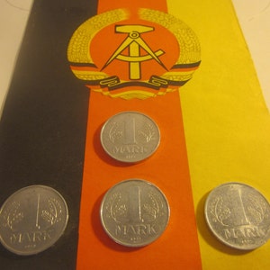 May include: Three silver coins with the inscription "1 Mark" on a yellow, black, and red flag with a symbol of a compass and hammer.