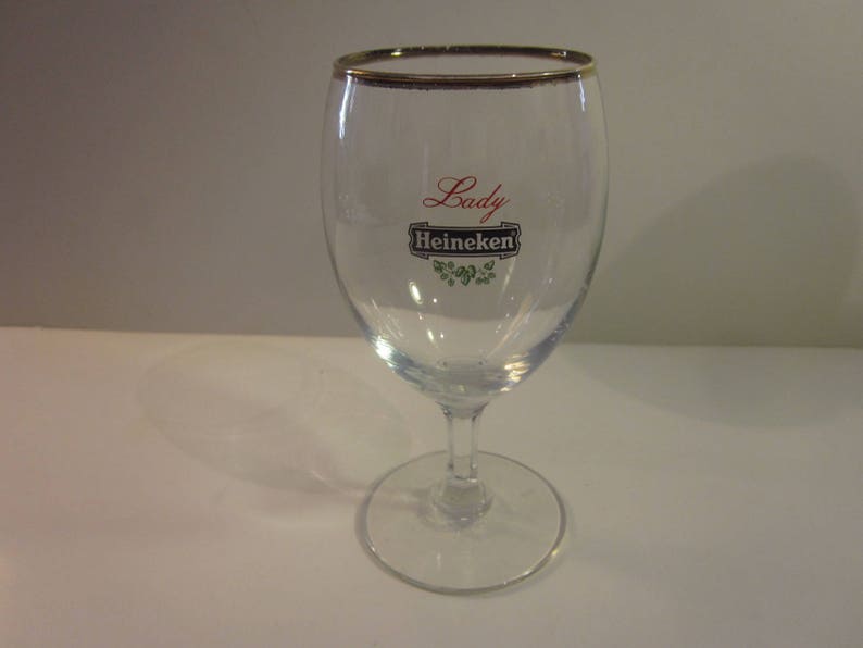 May include: A clear glass with a gold rim and the words "Lady Heineken" printed on the side.