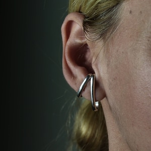 May include: A pair of silver ear cuffs, one is a simple hoop and the other is a curved, open design.