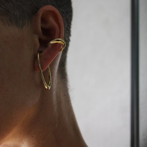 May include: A gold ear cuff with a curved, open design. The cuff is worn on the upper part of the ear.