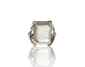 May include: A silver ring with a large, rectangular, iridescent white gemstone set in a decorative, ornate setting.