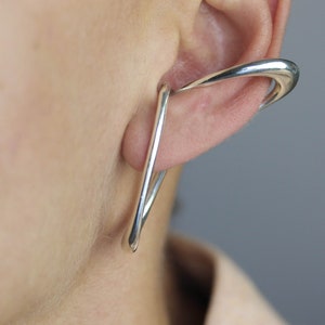 May include: Silver ear cuff with a curved, open design. The cuff is worn on the upper part of the ear.