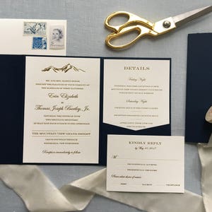 May include: A navy blue and ivory wedding invitation with gold foil lettering. The invitation features a mountain range design and the text "Erin Elizabeth to Thomas Joseph Bentley, Jr. Saturday, the twelfth of June, two thousand twenty-three at half past four o'clock in the afternoon The Mountain View Grand Resort, Grand Fontaine Terrace, Waterville, New Hampshire Reception immediately to follow Details Friday Night Informal Welcome Reception 6-8pm Mountain View Grand Resort Saturday Night Cocktail Hour 5:30-6:30pm Mountain View Grand Resort Dinner 6:30-8:00pm Mountain View Grand Resort Kindly Reply by May 1st, 2023"