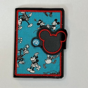 Peut inclure: Un petit portefeuille en tissu bleu avec un rabat en forme de tête de Mickey Mouse noir et des coutures rouges. Le portefeuille est orné d'un motif de personnages de Mickey Mouse en noir et blanc sur fond bleu.