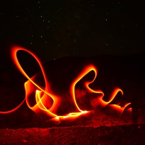 Peut inclure: Photographie à longue exposition de traînées lumineuses orange-rouge sur fond de ciel étoilé. Les traînées forment des formes abstraites. Le fond est sombre, avec des étoiles visibles.