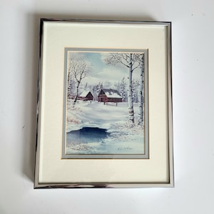 May include: Framed watercolour painting of a winter scene with two red barns in a snowy forest. The painting is signed "R.D. Allen" in the bottom right corner.