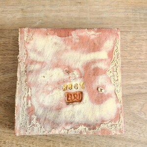 May include: A square, terracotta-colored tile with a white glaze. The tile has a rough, textured surface and a small, rectangular, orange and yellow design in the center. The design reads "B907".