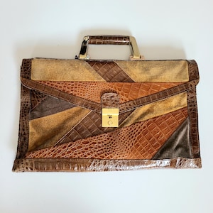 May include: A vintage briefcase with a patchwork design in shades of brown, tan, and beige. The briefcase features a gold-coloured clasp and handle, and a textured crocodile-like pattern.